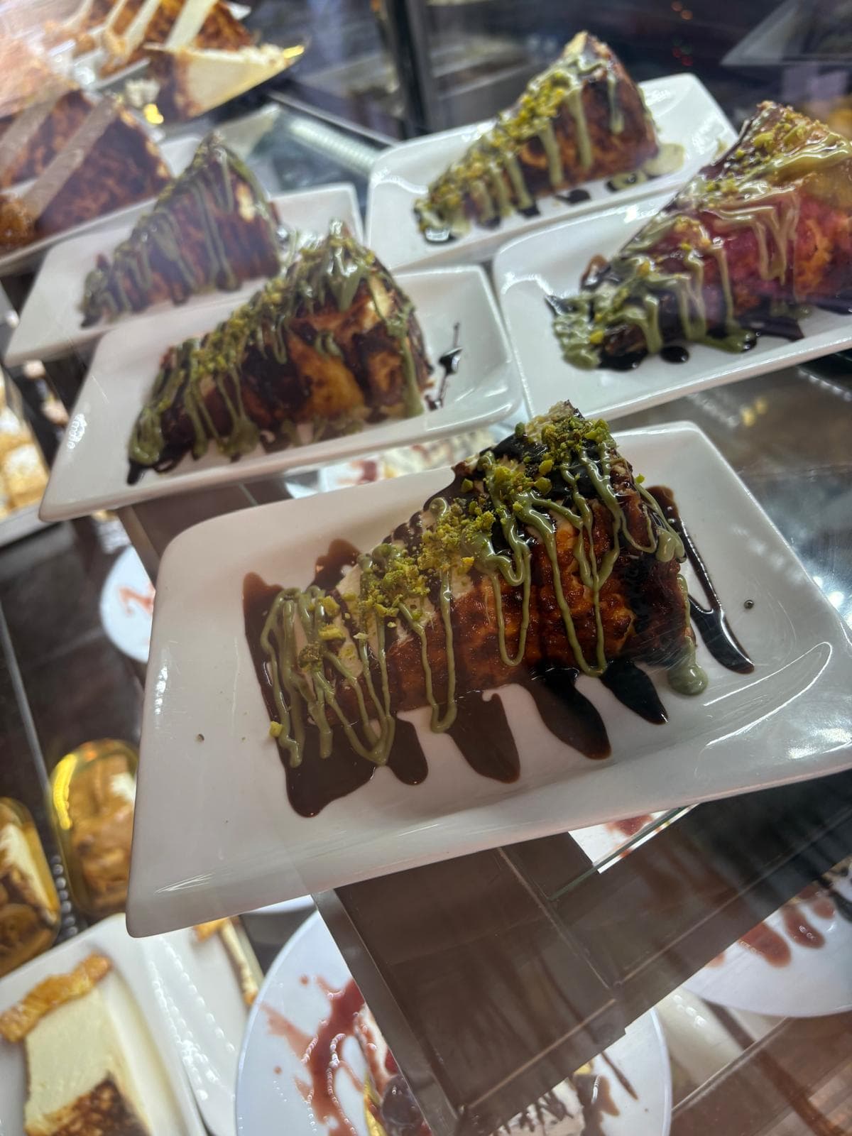 Stücke Cheesecake Pistazie mit Pistaziencreme und Schokoladensoße in der Vitrine